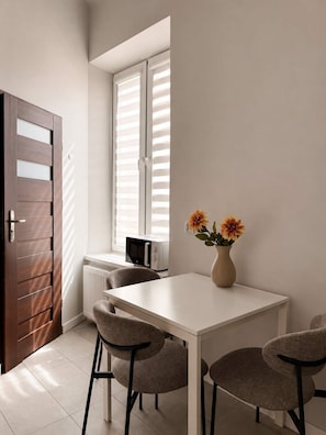 A dining area with a white table, four chairs, a vase with flowers, a microwave, and a window with blinds. - Św. Gertrudy 5A.2 | Near Wawel Castle | Old Town (Kraków)