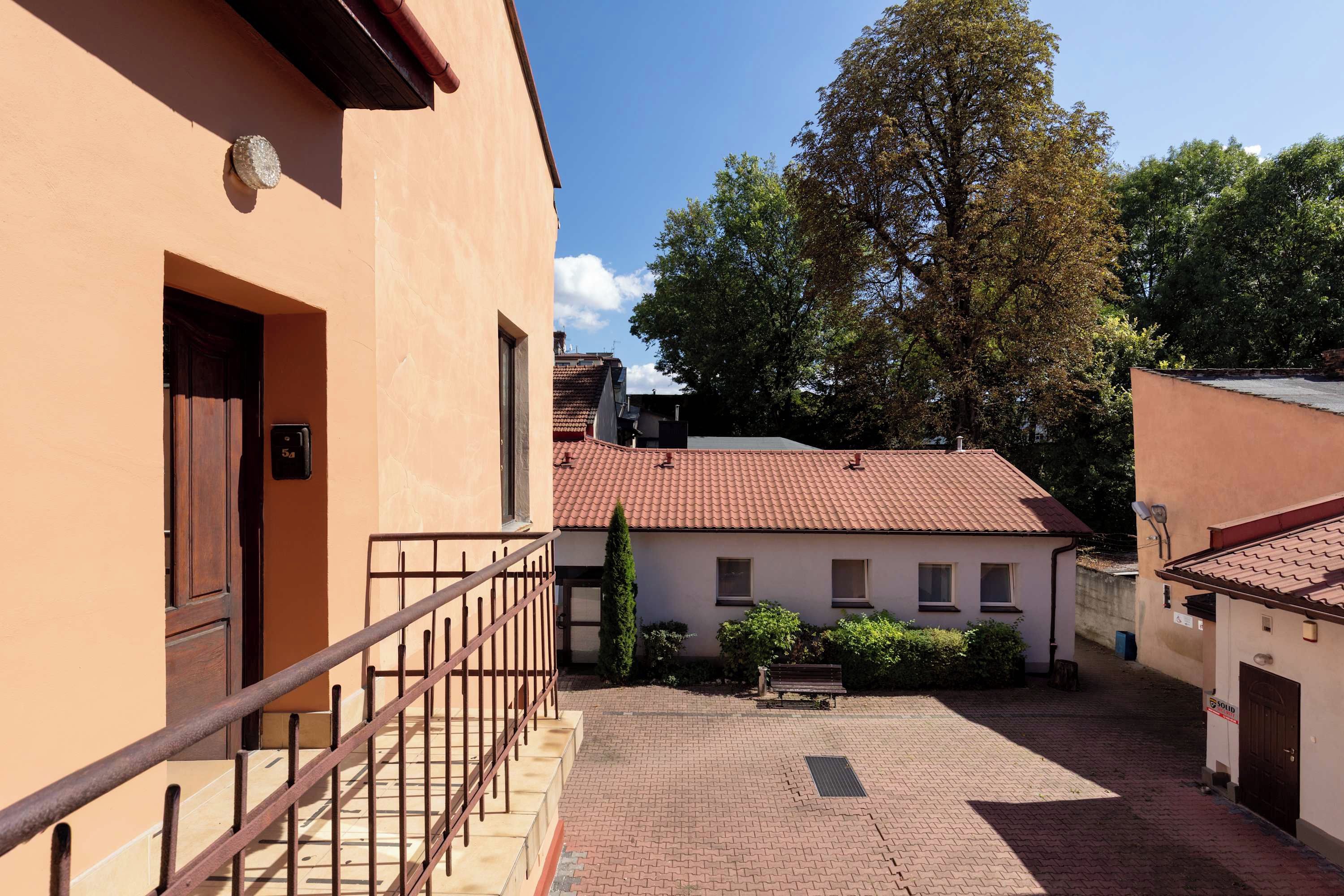 A courtyard with a paved walkway, a wooden door, and a metal railing.
