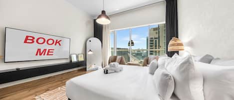 Une chambre d’hôtel moderne avec un grand lit, une vue sur la ville, une pancarte indiquant « RÉSERVEZ-MOI » et une grande fenêtre.
