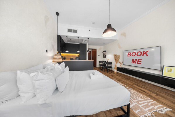Una camera d'hotel moderna con un letto grande, un'area pranzo e un cartello con su scritto 'BOOK ME'.