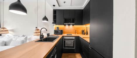 A modern kitchen with a wooden countertop, black appliances, and pendant lighting.