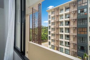 A view from a balcony with a metal partition, overlooking a multi-story building with balconies and air conditioning units. - Utopia Dream U2 Prestige Suites & Pool (Mueang Phuket)