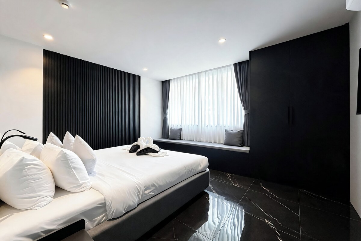 A modern bedroom with a bed, pillows, a window with curtains, and a dark wall.
