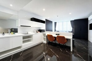 A modern kitchen with white cabinets, a black countertop, and a large mirror. There are two orange chairs, a sink, and a window with curtains. - Utopia Dream U2 Prestige Suites & Pool (Mueang Phuket)