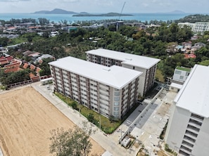 Un edificio residencial de varios pisos con techo plano, rodeado de vegetación y una zona arenosa.
