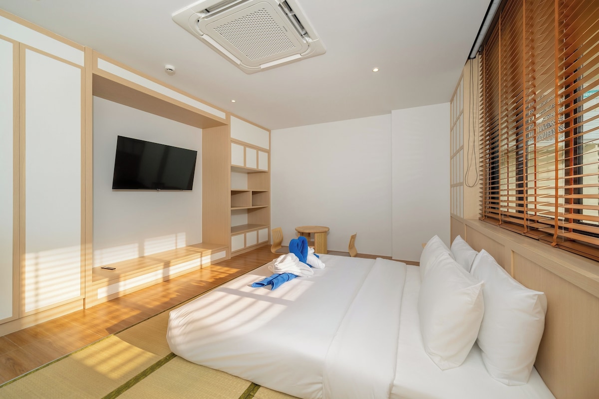 Un dormitorio moderno con una cama grande, un televisor en la pared y una ventana con persianas.