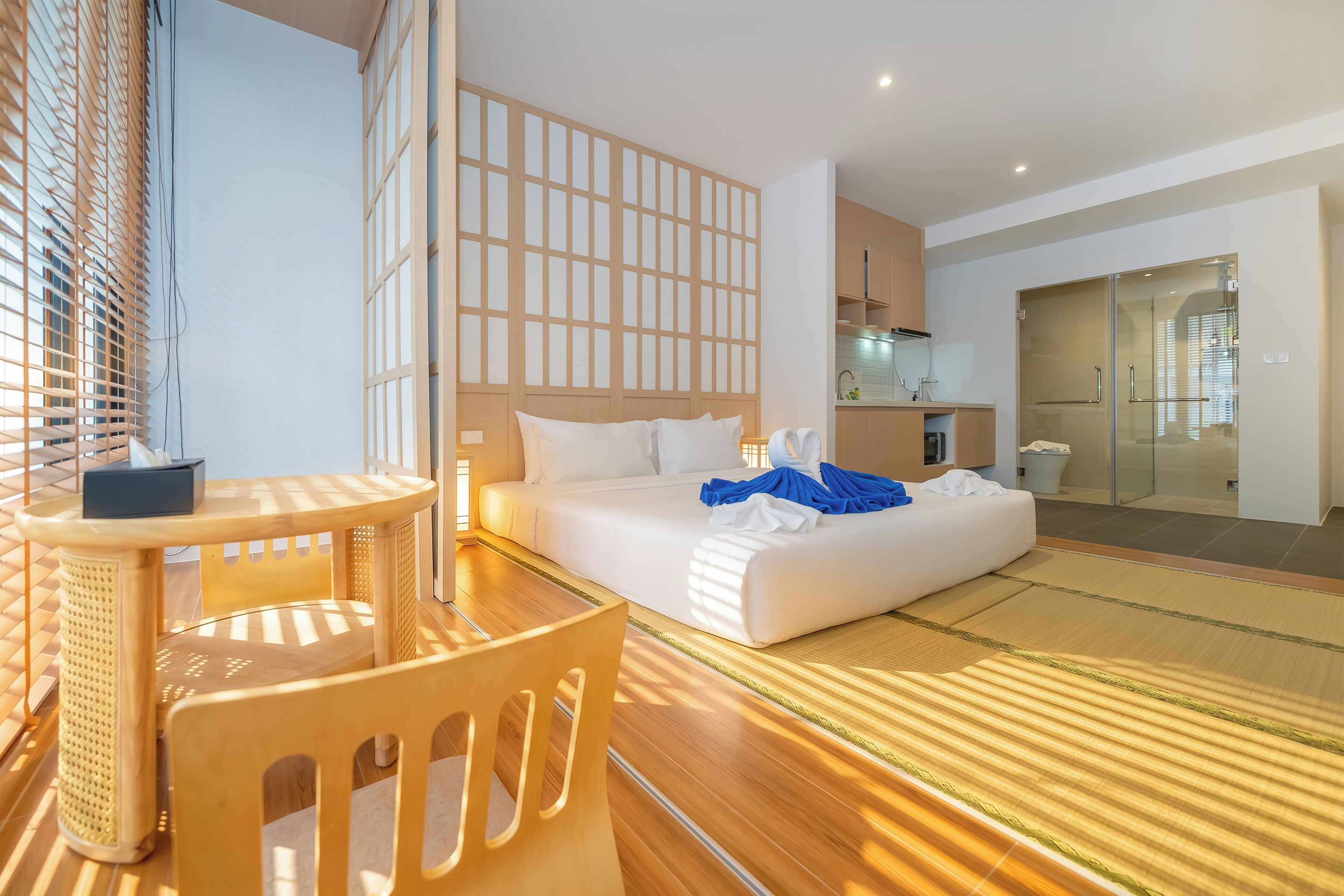 Une chambre d’hôtel comprenant un lit, une petite table, une chaise, un coin cuisine et une cabine de douche en verre.