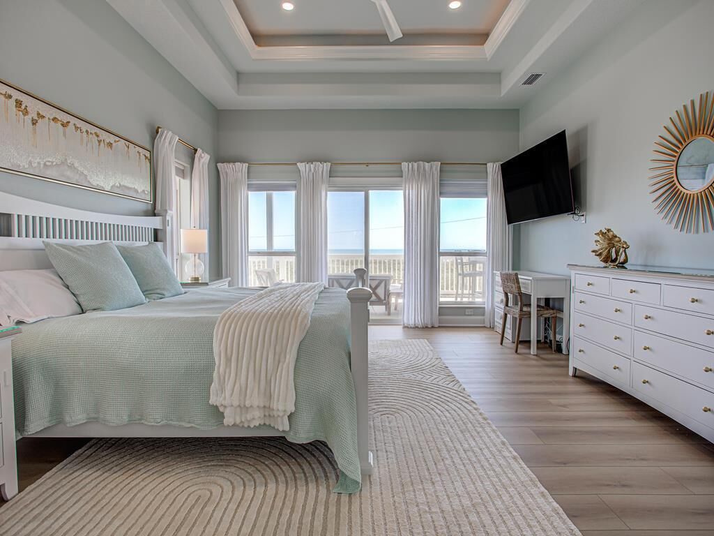 A bedroom with a large bed, a TV, a dresser, and a balcony with curtains.