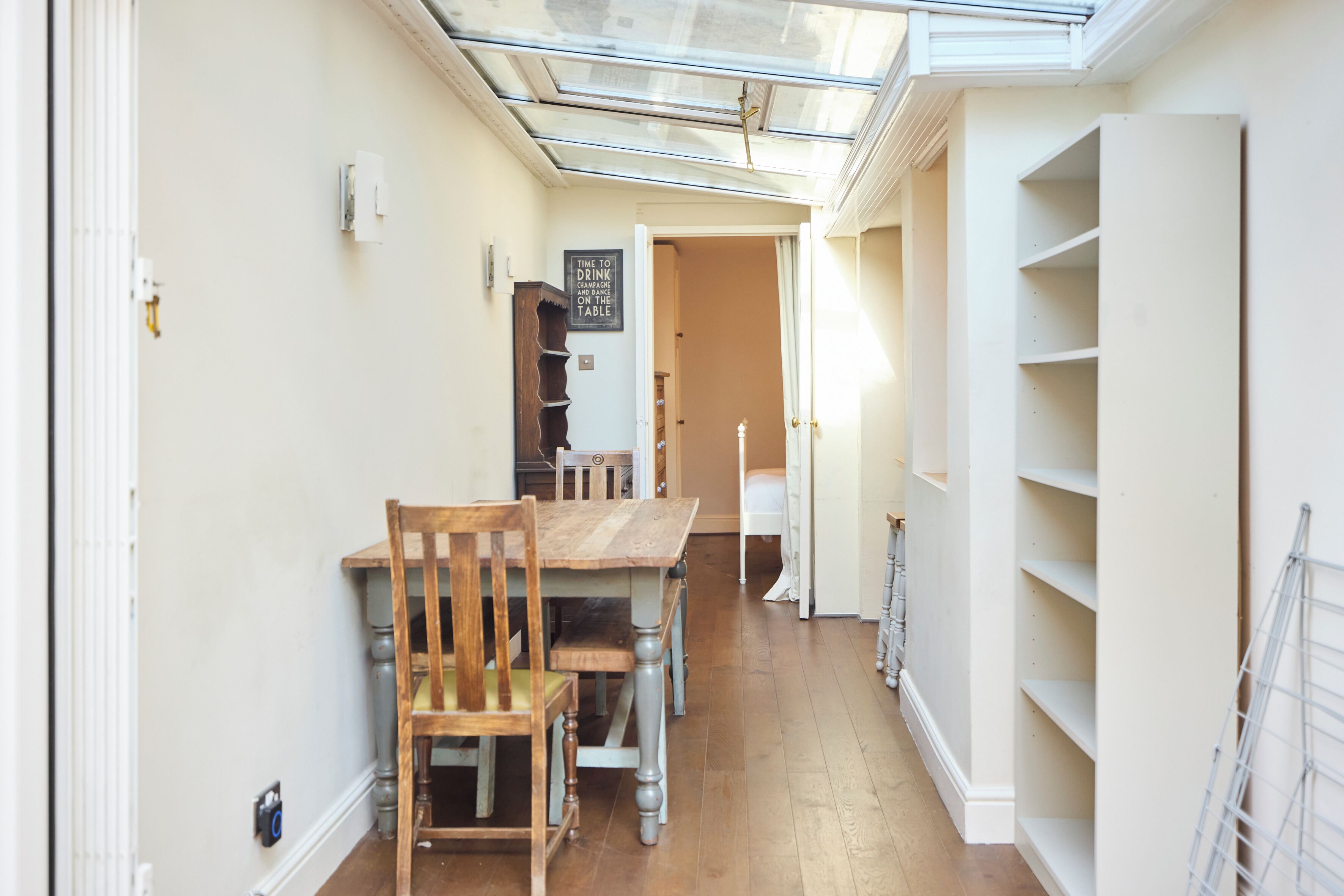 A narrow hallway with a wooden dining table and chairs, a white radiator, and a glass ceiling.