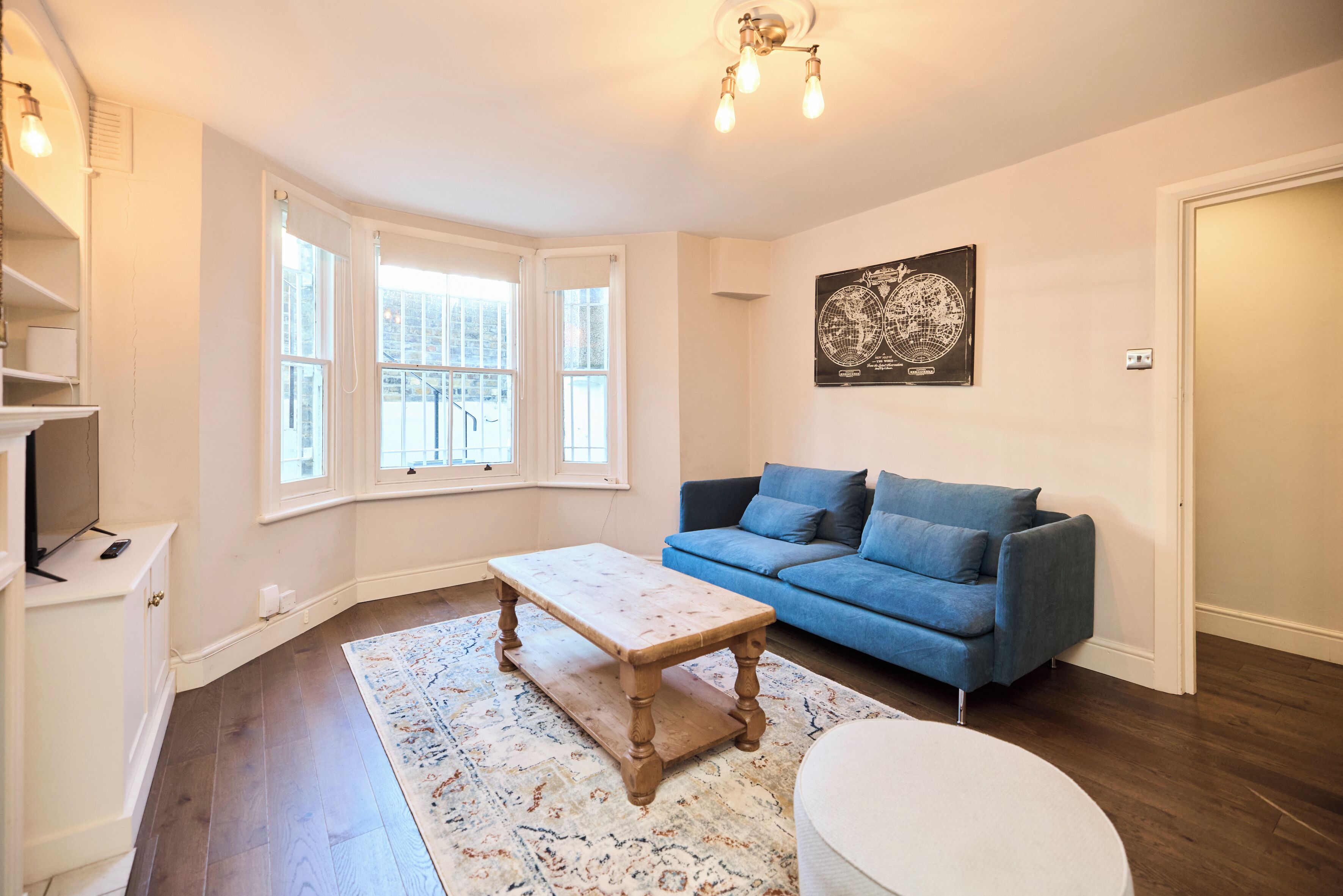 A living room with a blue sofa, a wooden coffee table, a patterned rug, and a globe artwork on the wall.