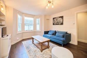 A living room with a blue sofa, a wooden coffee table, a patterned rug, and a globe artwork on the wall. - A Battersea State of Mind (London)