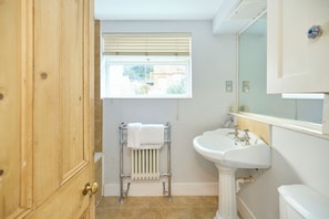 A bathroom with a wooden door, a window with blinds, a radiator, a sink, and a toilet. - A Battersea State of Mind (London)