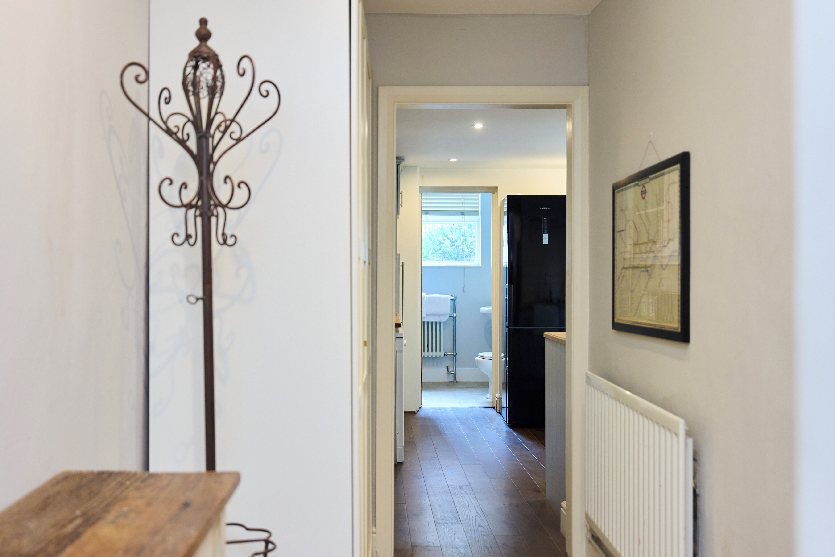 A hallway with a radiator, a framed map on the wall, and a door leading to a bathroom.
