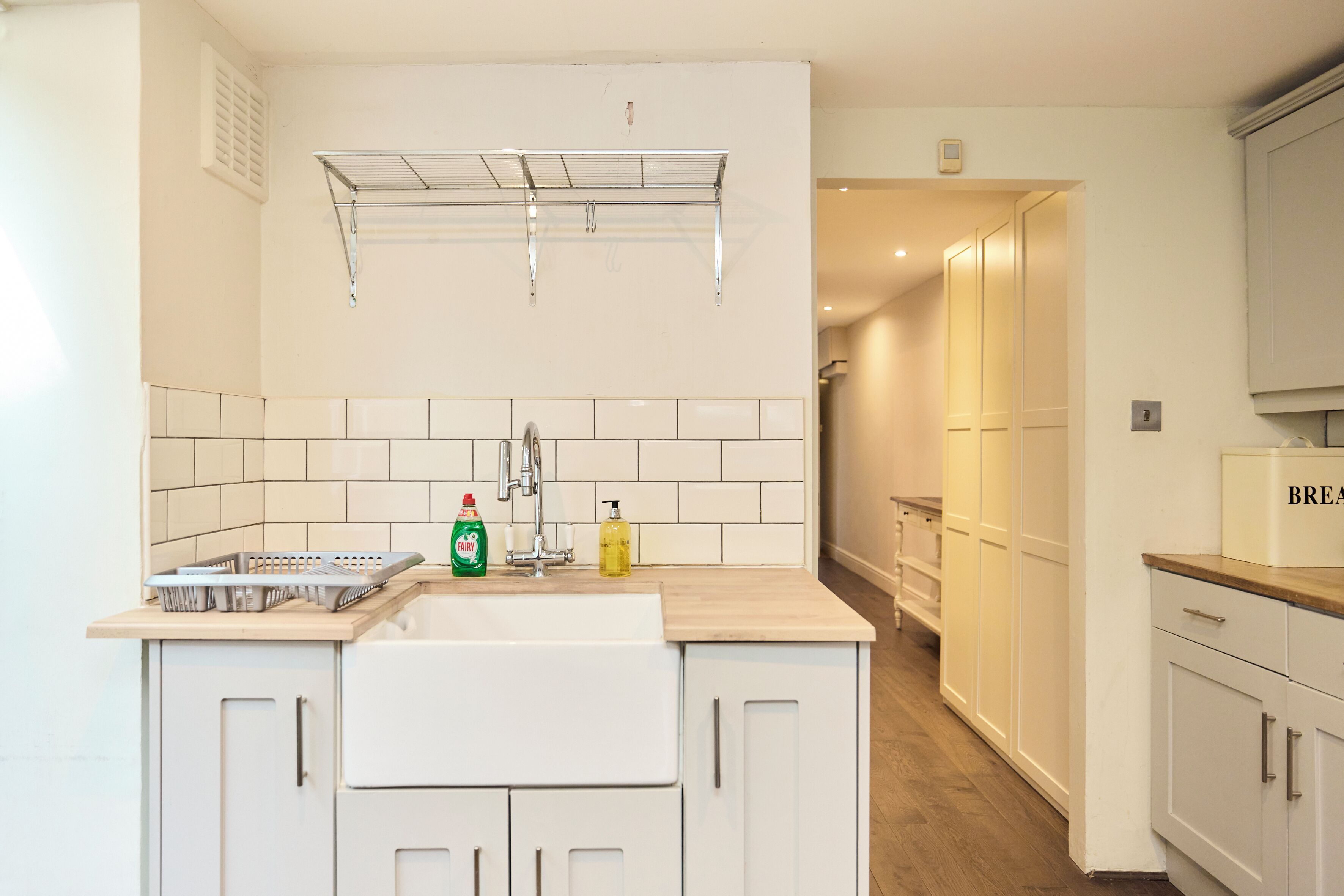 A kitchen with a sink, drying rack, and cabinets.