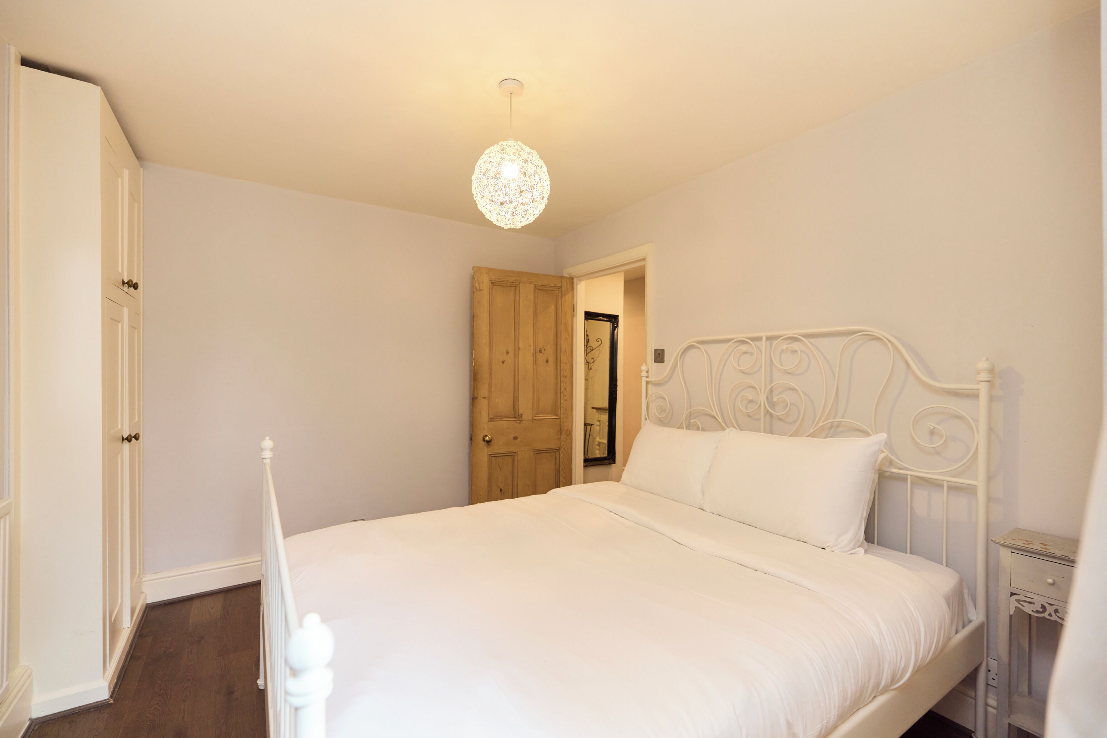 A bedroom with a white bed, a wooden door, and a white radiator.