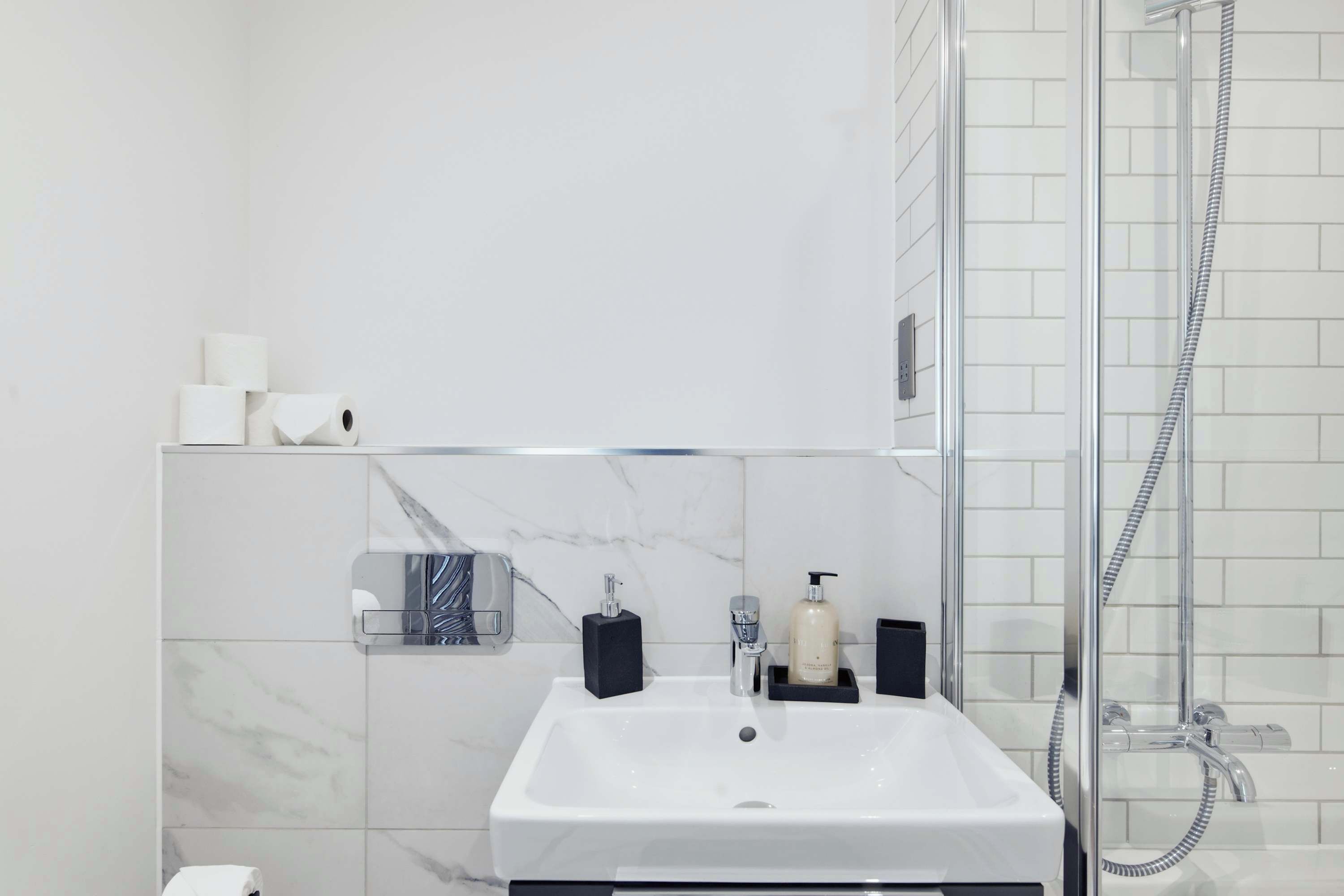 A modern bathroom with a white sink, a handheld showerhead, and a glass-enclosed shower.