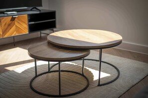 Two round wooden tables with metal legs on a textured rug in a room with a TV and a wooden cabinet. - Modern 1 Bedroom Apartment in Central Birmingham (Birmingham)