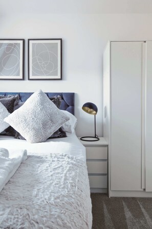 Ein Schlafzimmer mit einem Bett, einem Nachttisch mit Lampe, einem Kleiderschrank und zwei gerahmten abstrakten Kunstwerken an der Wand.
