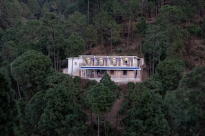 Un bâtiment à deux étages entouré d’une forêt dense, avec un balcon à l’étage supérieur.