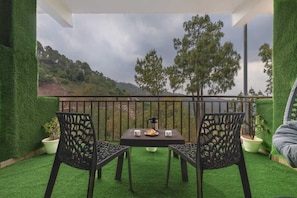 Un balcon avec une table et des chaises, une vue sur un paysage vallonné et des plantes en pot.