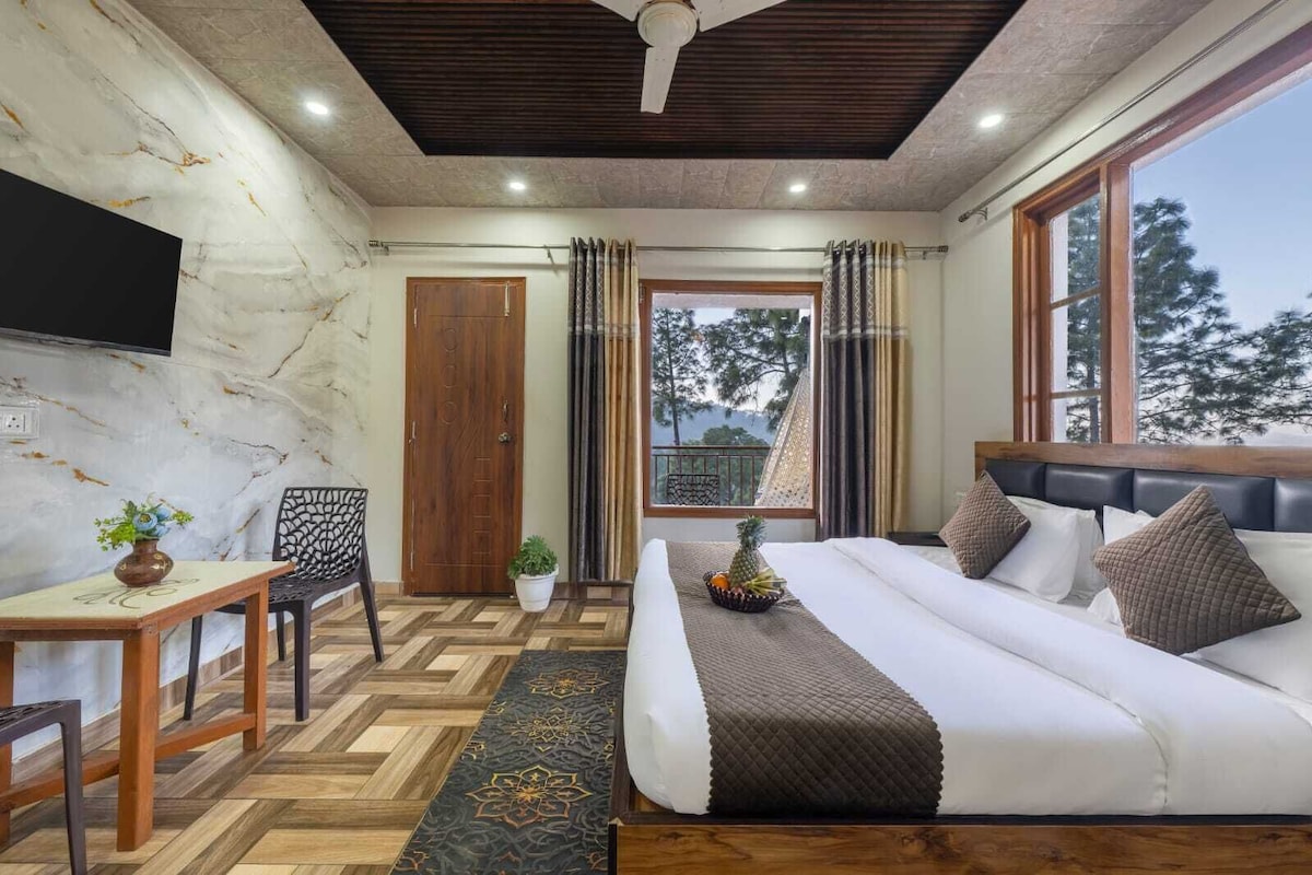 Une chambre à coucher comprenant un lit, un bureau, une chaise, un téléviseur et une fenêtre donnant sur des arbres.