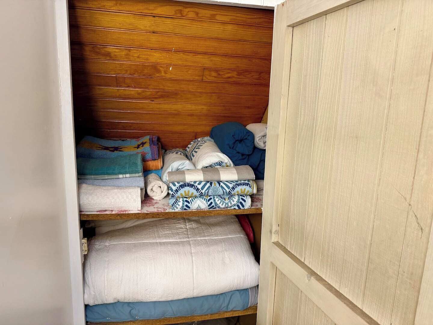A closet with wooden shelves holding folded blankets and pillows.