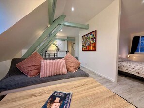 Una moderna camera da letto mansardata con un soffitto spiovente, un tavolo in legno con una rivista, un divano con cuscini e un quadro astratto dai colori vivaci appeso al muro.