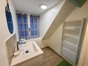 Un bagno piccolo con un lavandino bianco, uno specchio, una finestra con tende e un termosifone.