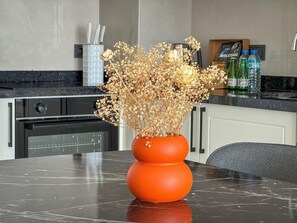 Eine Küchenzeile mit Marmorarbeitsplatte, eine Vase mit Trockenblumen und ein 'WELCOME'-Schild an der Wand.
