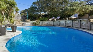 Una piscina de borde curvo, rodeada por una valla de madera y plantas en macetas.