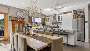 Una cocina moderna con comedor, muebles blancos, una araña y vistas al exterior.