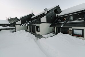 A modern two-story building with a sloped roof covered in snow, surrounded by snowbanks.