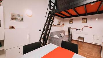 A room with a dining table, a gray sofa, a ladder, and a wooden ceiling.