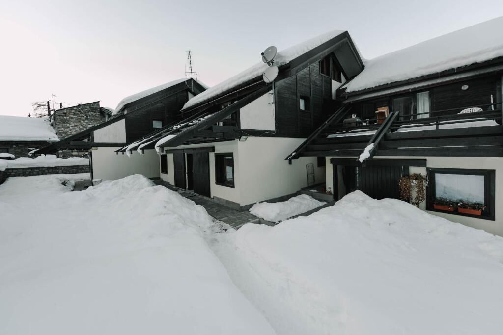 A modern house with a sloped roof covered in snow, surrounded by snowbanks.