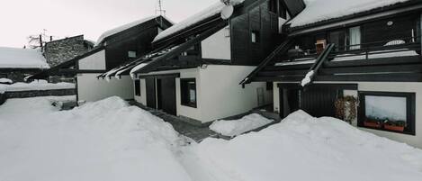 A modern house with a sloped roof covered in snow, surrounded by snowbanks.