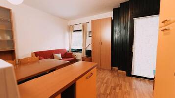 A compact living space with a kitchenette, a red sofa, wooden cabinets, and a sliding door.