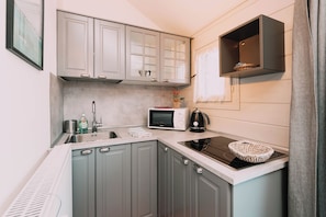 A compact kitchen with grey cabinets, a microwave, a kettle, and a small shelf.