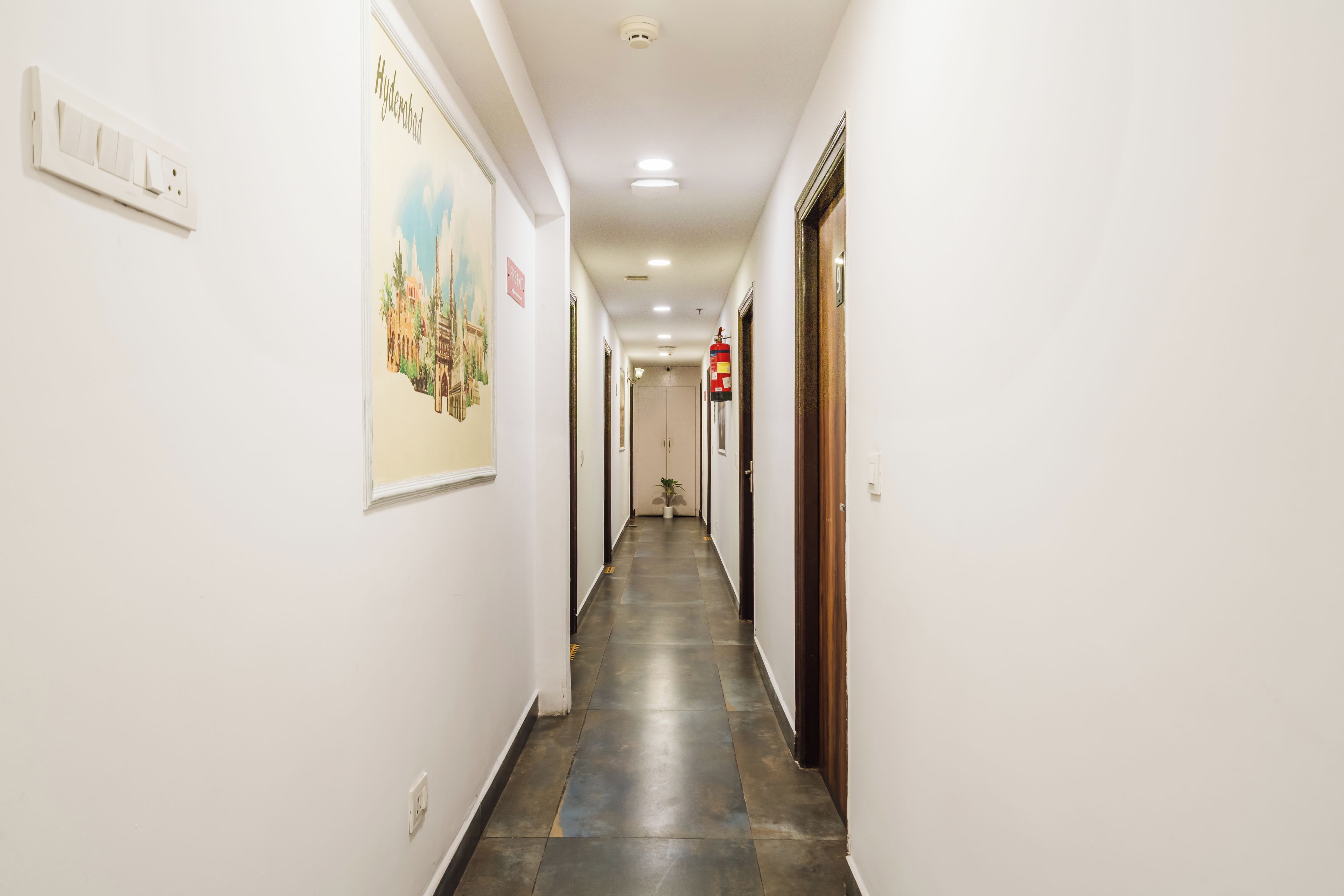 Pasillo de hotel con extintor montado en la pared, un letrero que dice 'PREFECT' y un cuadro de un edificio.