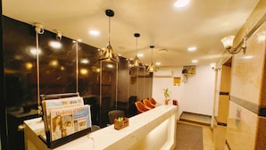 Recepção de hotel com balcão de mármore, assentos e iluminação pendente.