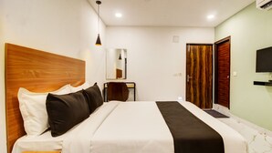 Quarto de hotel com cama, escrivaninha, cadeira, espelho, televisão e porta.