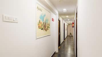 Corredor de hotel com sinalização de saída de incêndio, interruptor de luz na parede e quadro com imagem de um edifício.