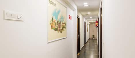A hotel corridor with a fire exit sign, a wall-mounted light switch, and a framed picture of a building.