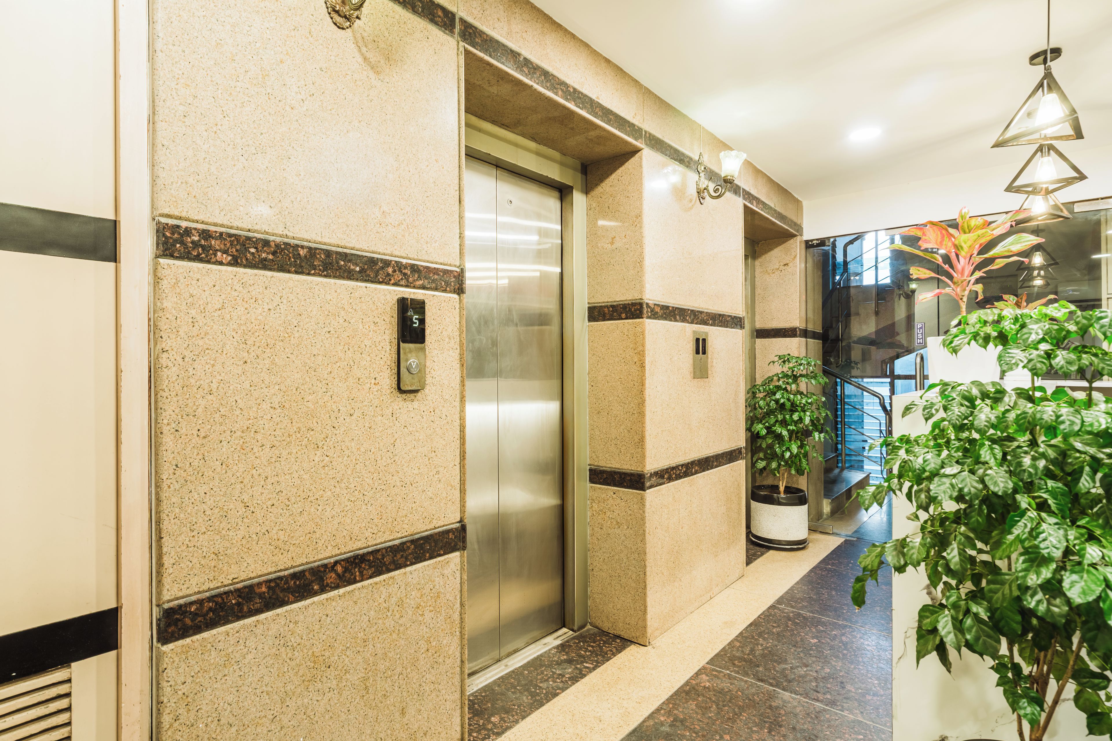 A modern elevator with a metallic finish, flanked by walls with speckled tiles and black borders.