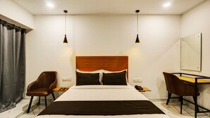 Quarto de hotel com uma cama, duas cadeiras, uma escrivaninha e um espelho.
