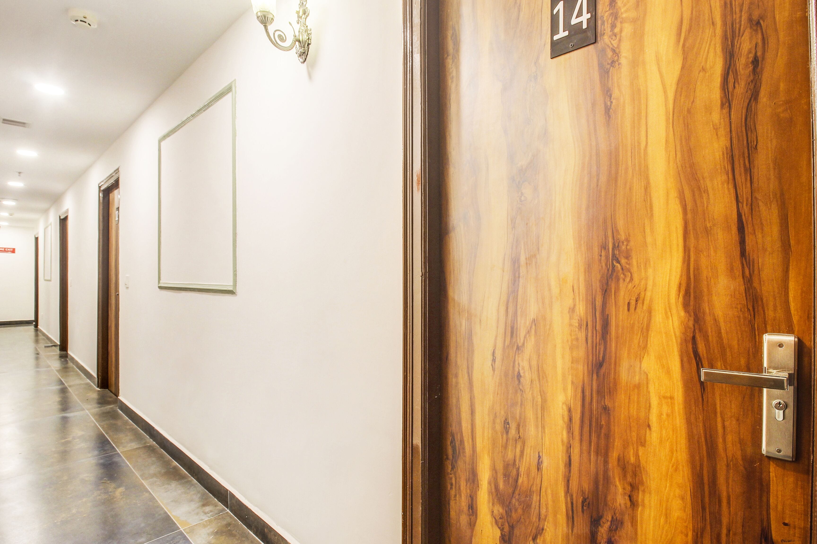 Un pasillo de hotel con una puerta de madera numerada 14, un cuadro enmarcado en la pared y un suelo de baldosas.