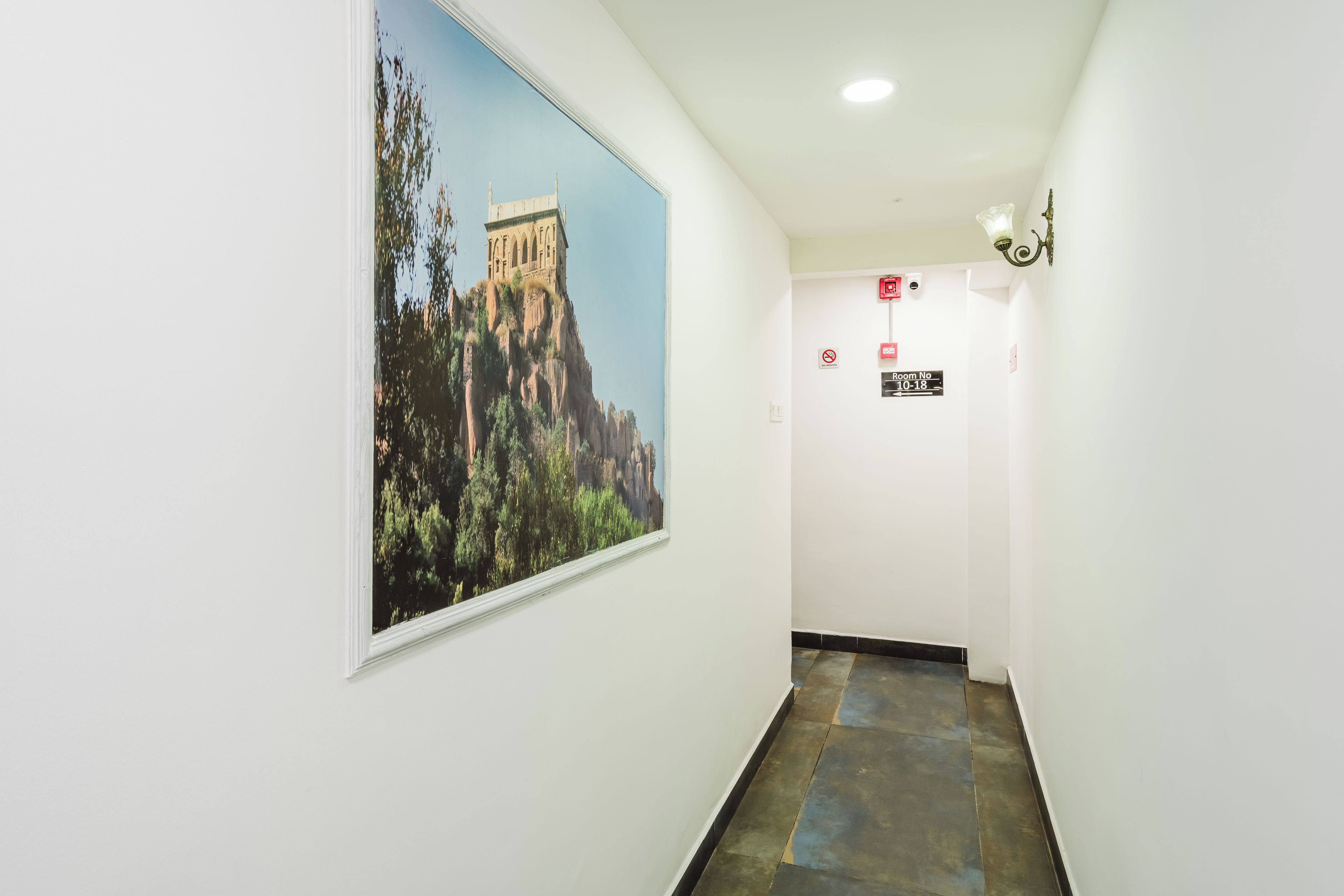 A hallway with a large framed picture of a building on the wall, a fire alarm, and a sign indicating room number 10-18.