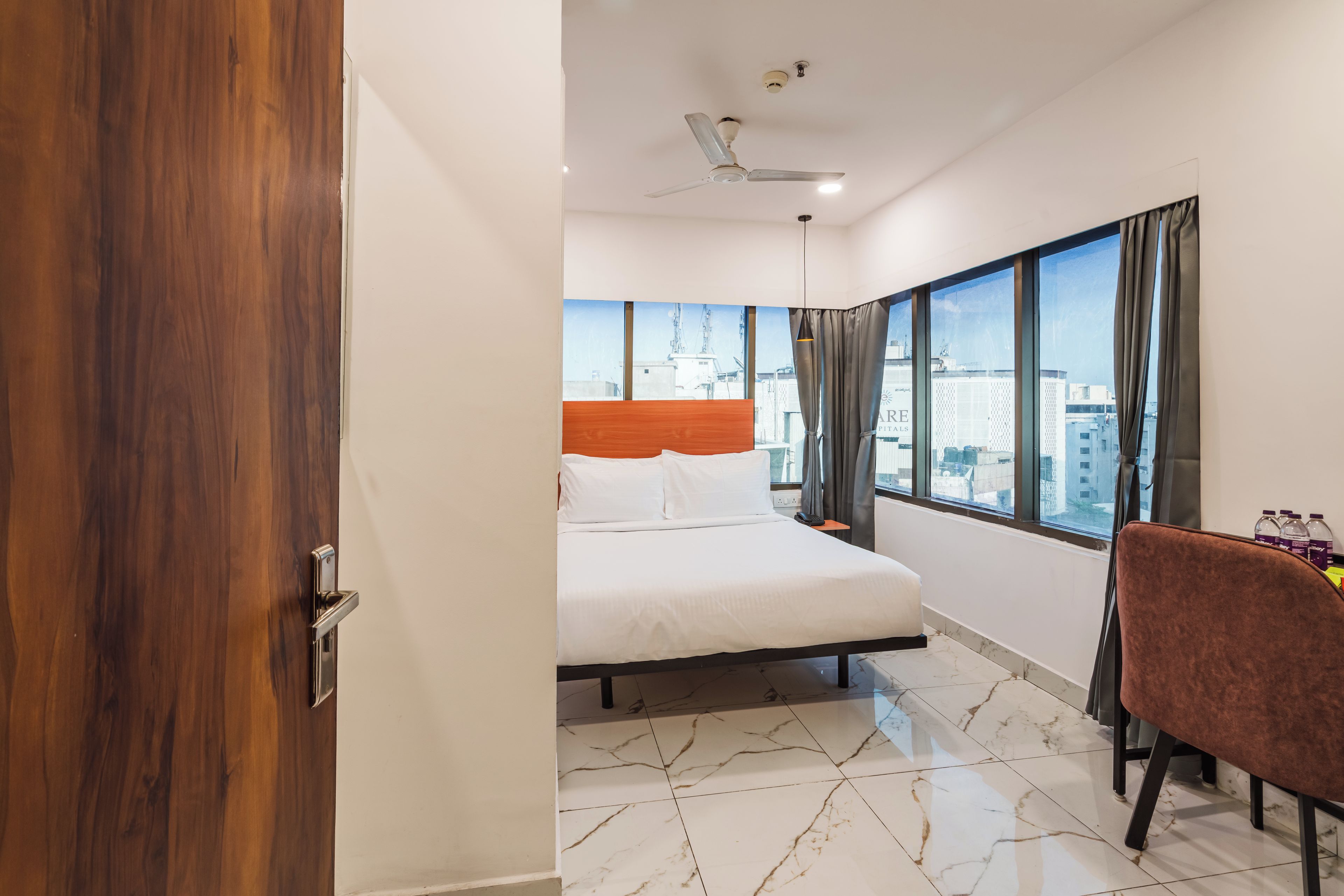 Una habitación de hotel con cama, una silla, ventana y vista a la ciudad, además de ventilador de techo.