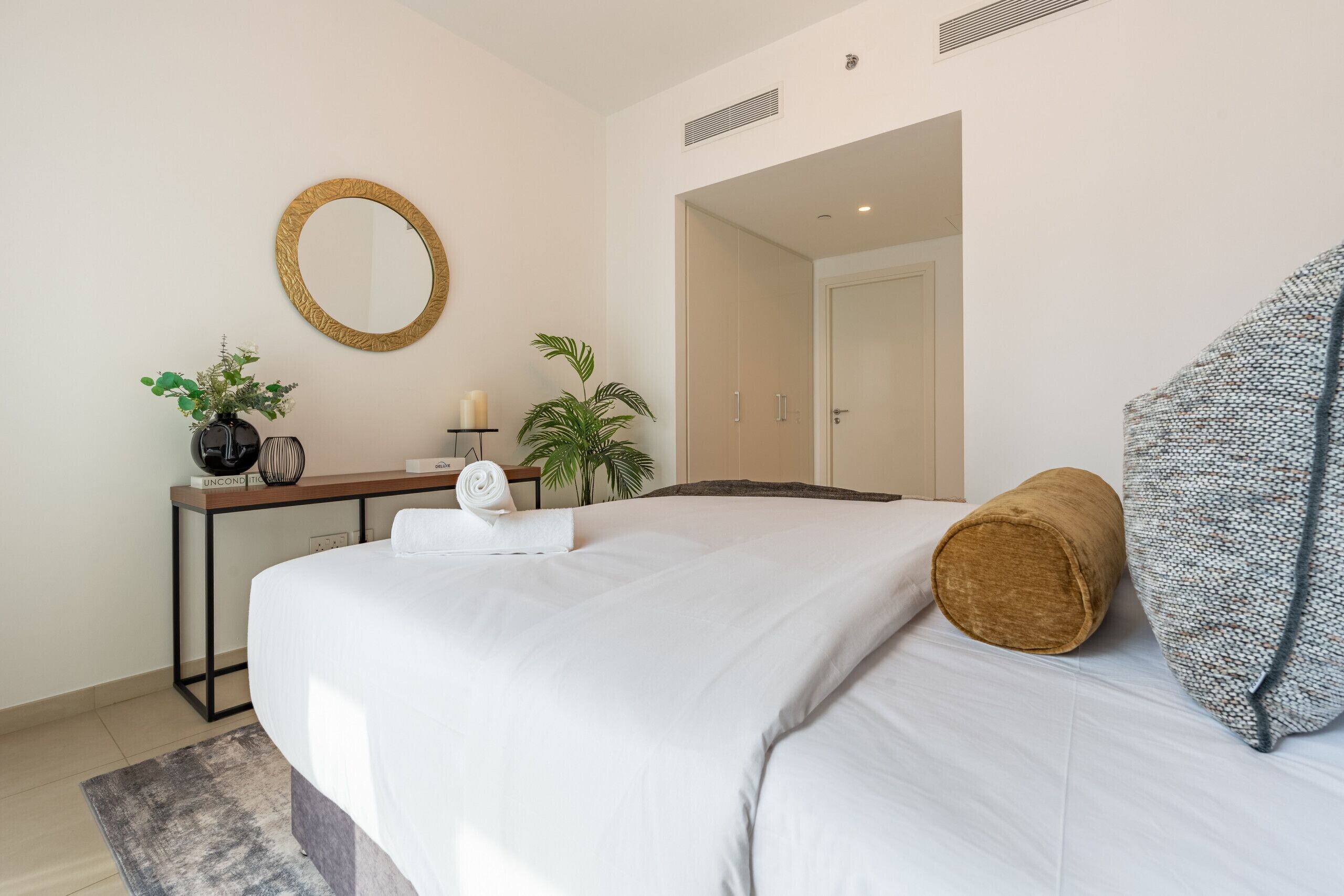 Habitació d'hotel amb un llit, una taula de treball, un mirall, una planta en test i una porta que dóna a una altra habitació.