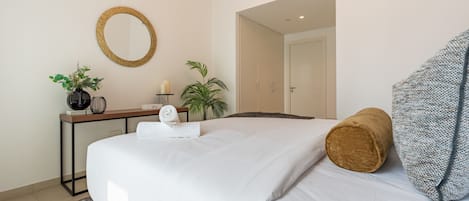 Habitación de hotel con cama, escritorio, espejo, planta en maceta y puerta que da a otra habitación.