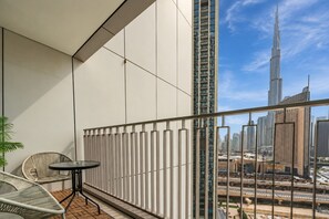A balcony with a view of a tall skyscraper, a round table, and two wicker chairs. - High-Floor 2BR with Balcony Framing Stunning Burj Khalifa Views,Near Dubai Mall (Dubai)